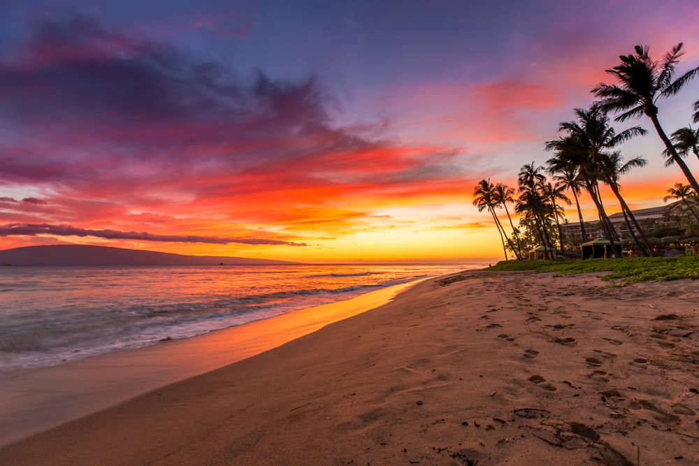 Vivid sunset over Kaanapali Beach with palm trees.