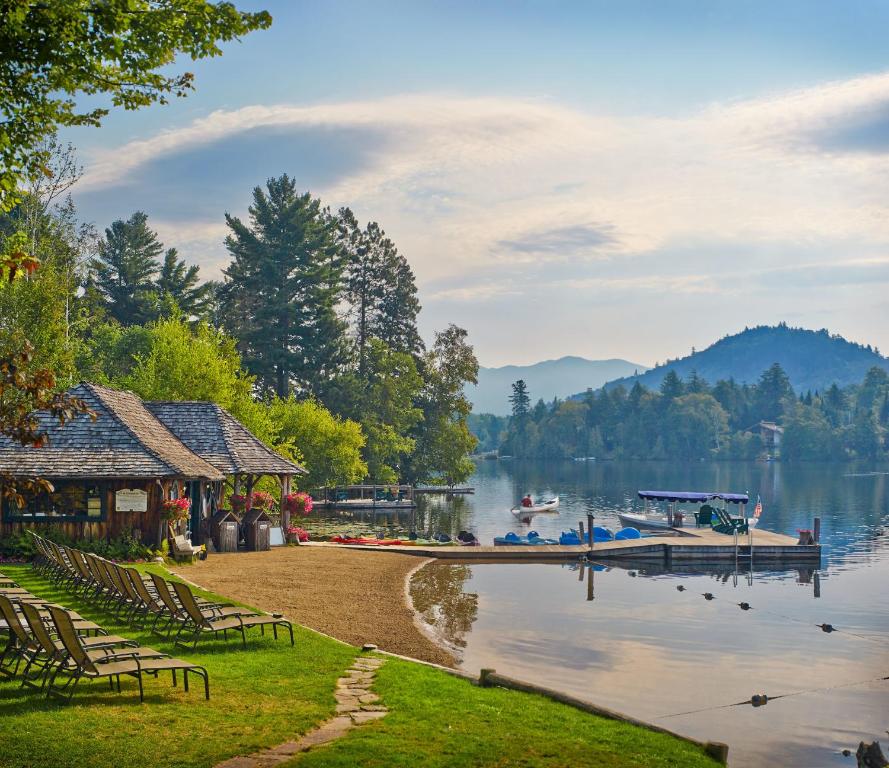 Picture showing a lke with moutinas in the background and a boathouse. There is a lawn with sunbeds on.  