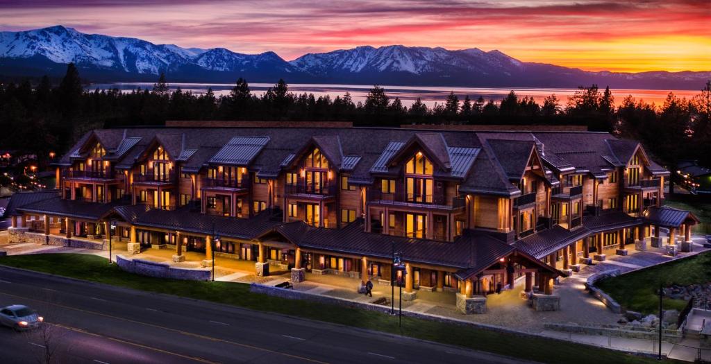 The view of a chalet style resort on the edge of a lake with mountains in the distance as the sun sets