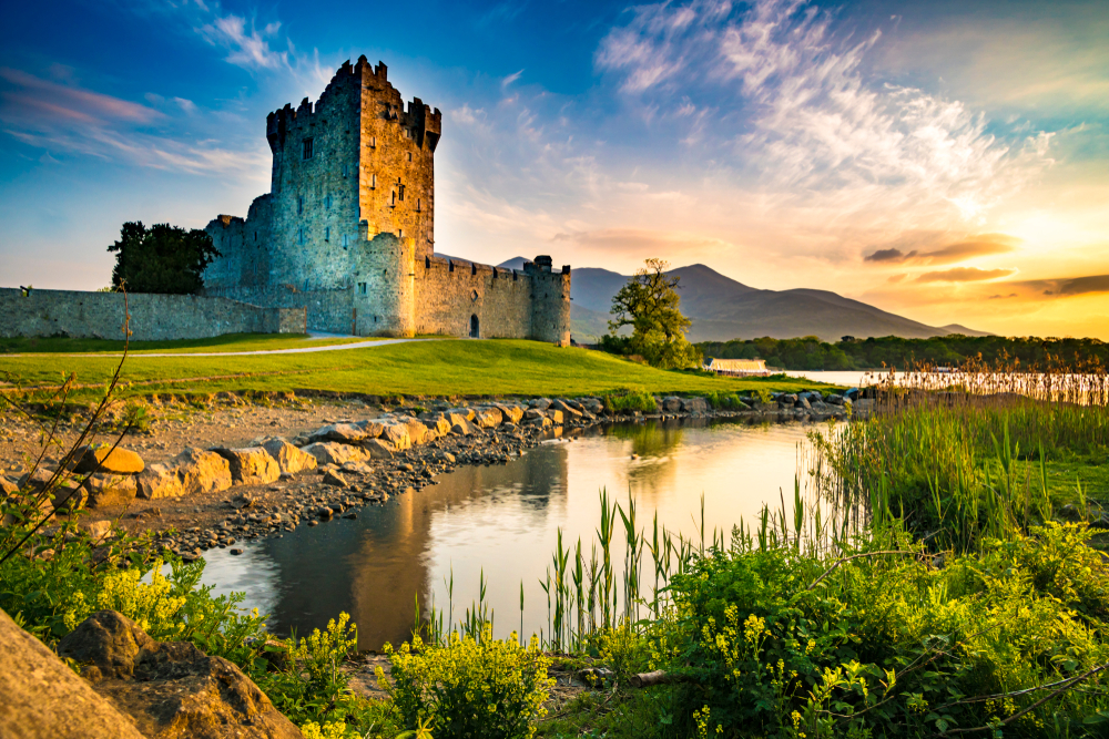 Golden hour over an old castle fortress beside a river with mountains in the distance during a trip to Ireland.