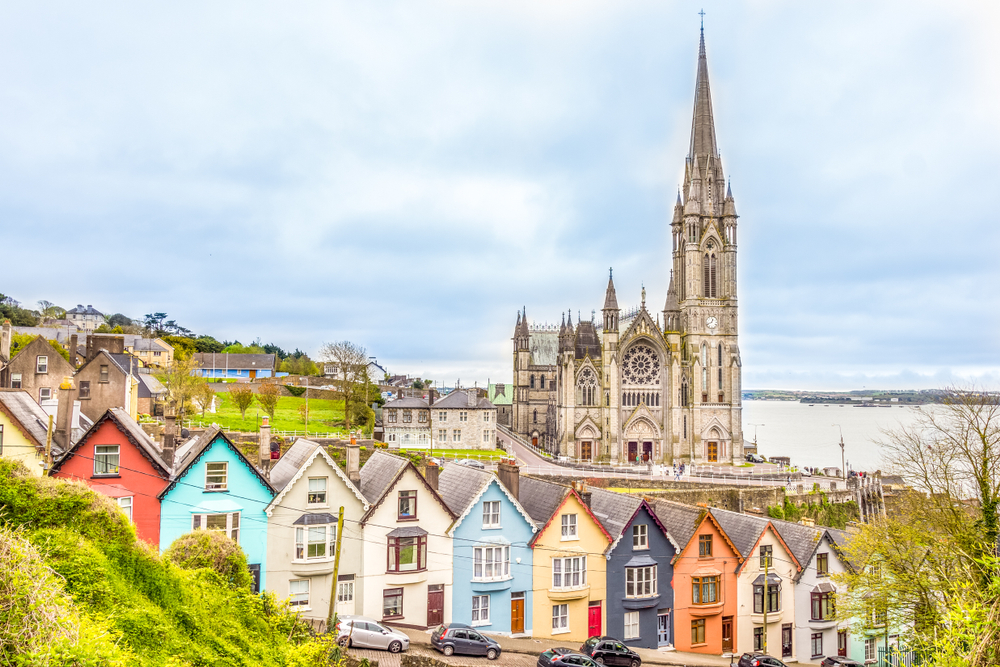Colorful houses line a street in Cobh, Ireland, with a grand cathedral in the background.