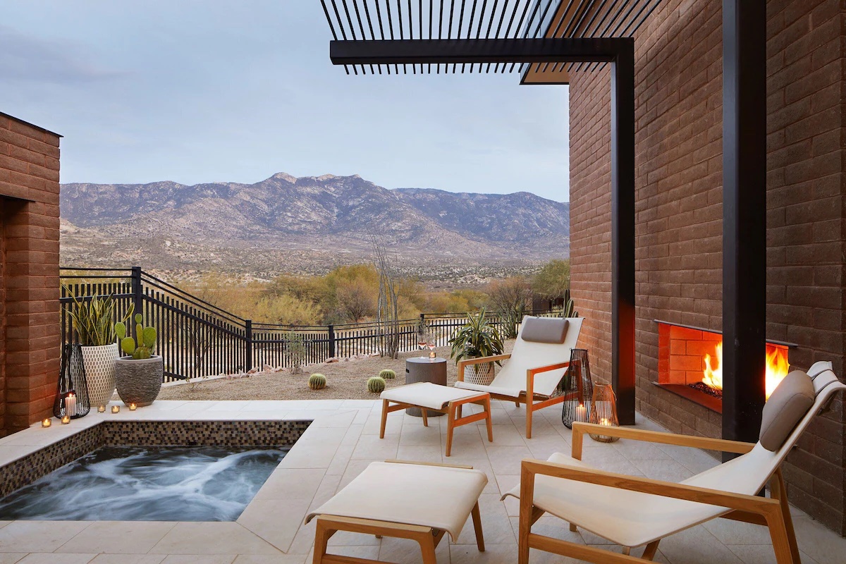 lounge chairs and a private hot tub with a fire going in a brick fireplace and mountains in the background