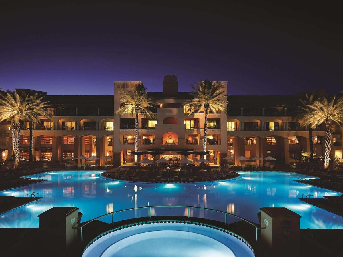 the pool lit up at nighttime at the Fairmont Scottsdale Princess with a handful of palm trees in front of the resort