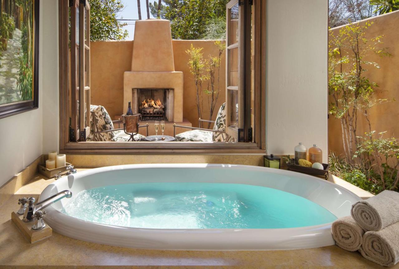 a soaking bat tub with windows open to the outdoors where there's a patio with champagne glasses and a fire going in the outdoor fireplace.