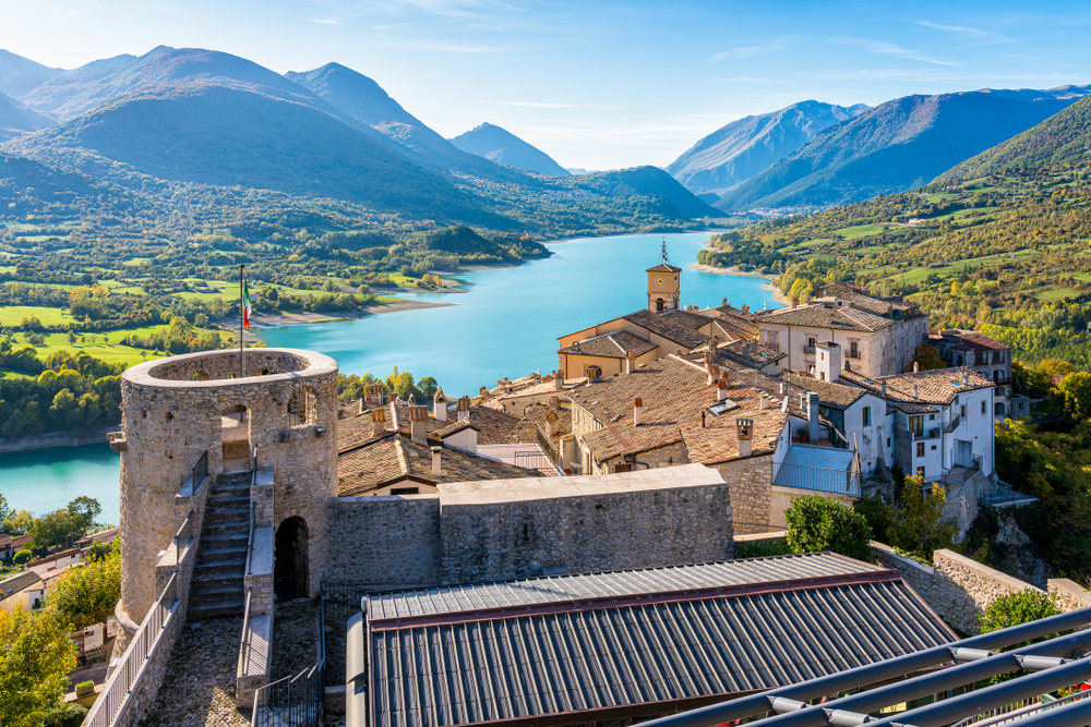 View looking over a medieval town to a lake and rolling mountains in Abruzzo, one of the best day trips from Rome.