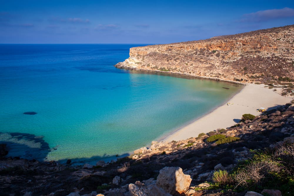 The horseshoe-shaped cove and blue water of Spiaggia dei Conigli in Lampedusa, one of the best beaches in Italy.