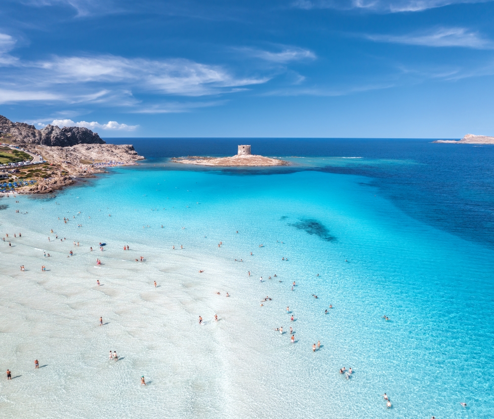 People wade in the shallow, sapphire waters of La Pelosa, one of the best beaches in Italy, on a sunny day.