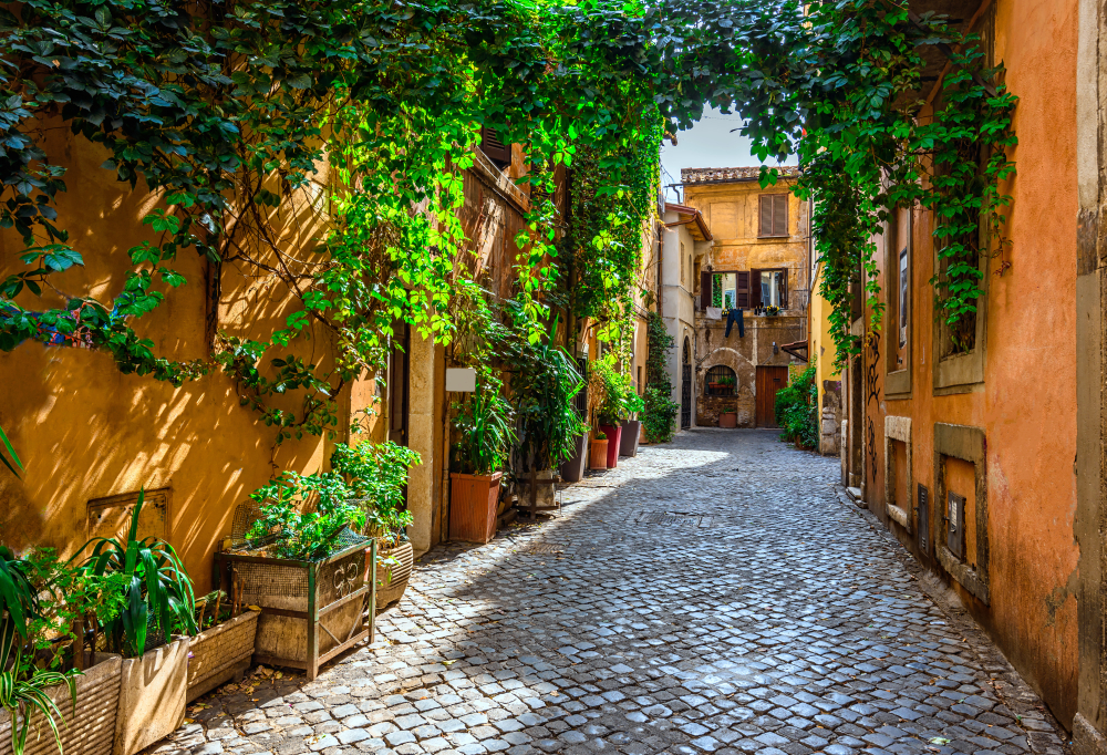 A cobblestone alley with orange buildings covered in vines.