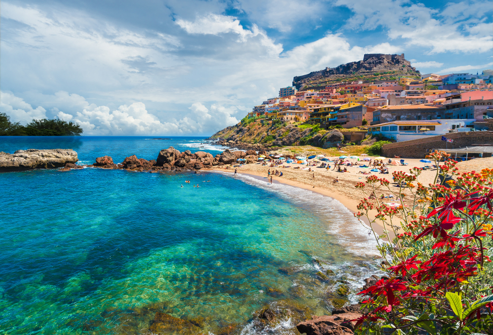 Beach next to colorful water and flowers in Castelsardo, one of the best beach towns in Italy.