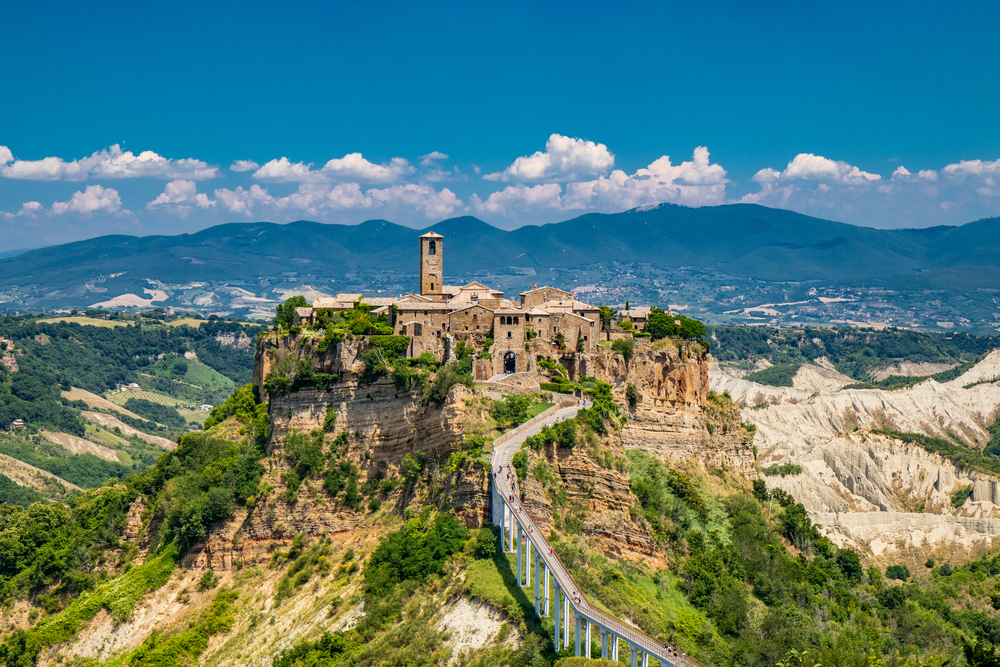 Aerial view of the hilltop town of Civita di Bagnoregio with a mountain vista in the distance.