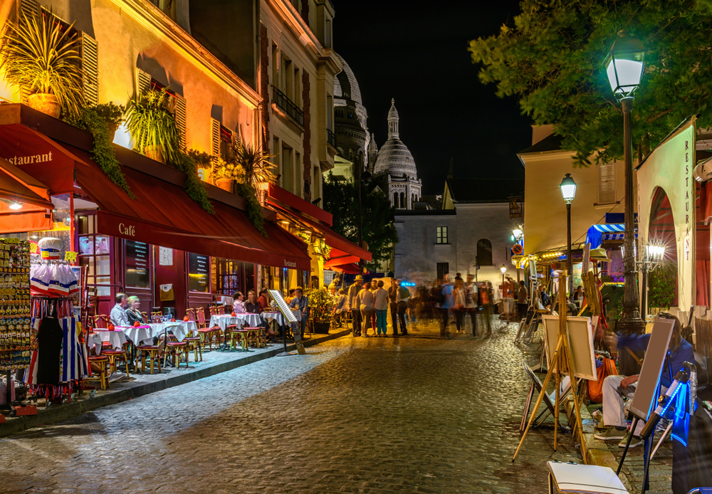 A street in Montmartre with restaurants on one side and painters on the other at night.
