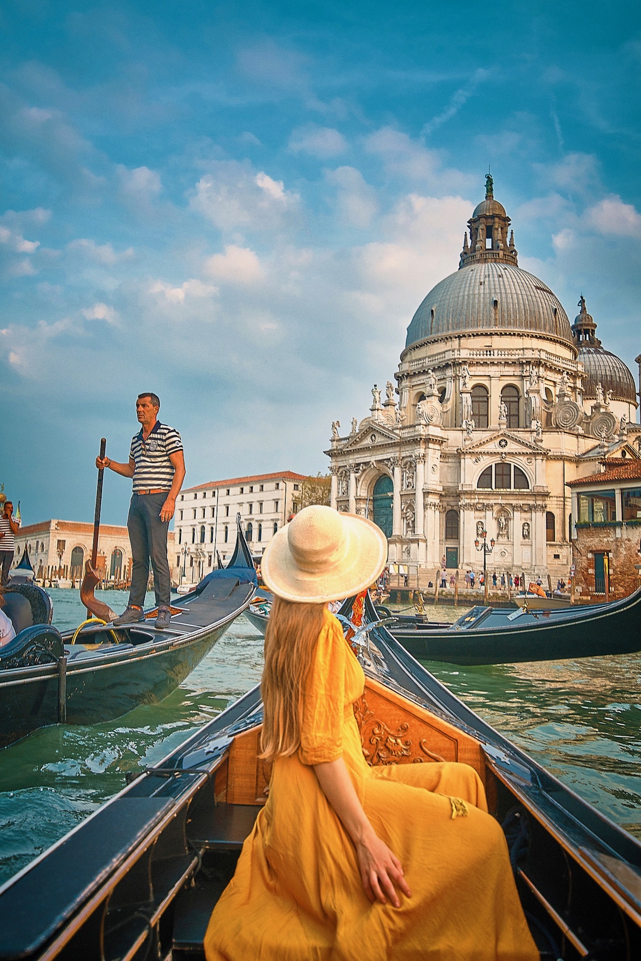 Woman in a yellow dress and sun hat rides in a gondola on the Grand Canal of Venice, Italy.