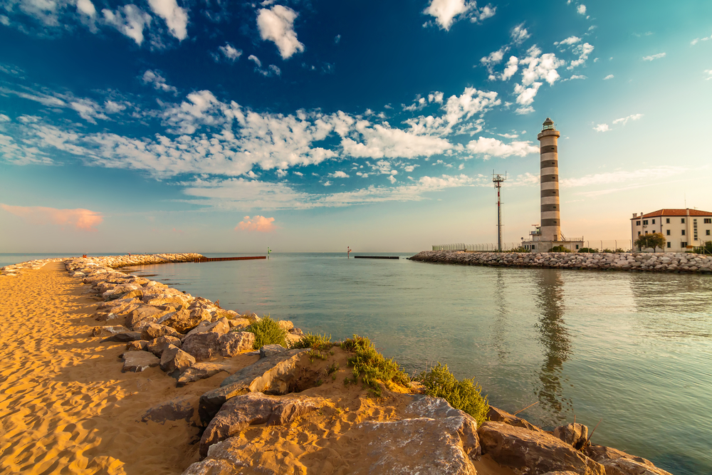 Golden hour over a black and white striped lighthouse at the beach at Lido di Jesolo.