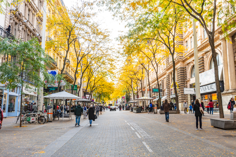 People walking along the shopping street in the Mariahilf district under yellow trees.