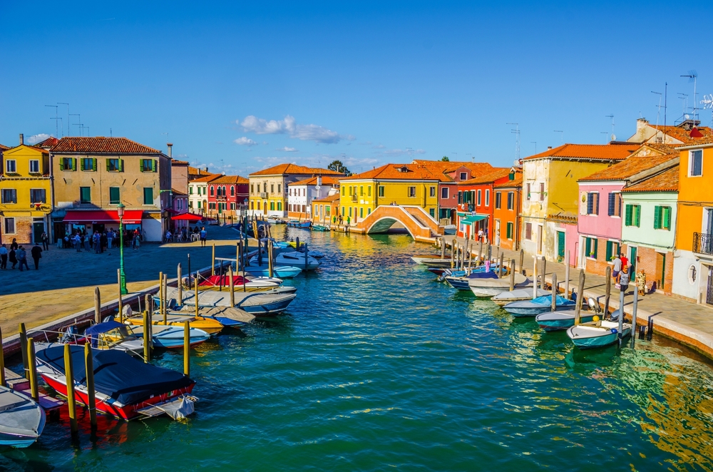 Colorful houses on the island of Murano line a canal with boats.