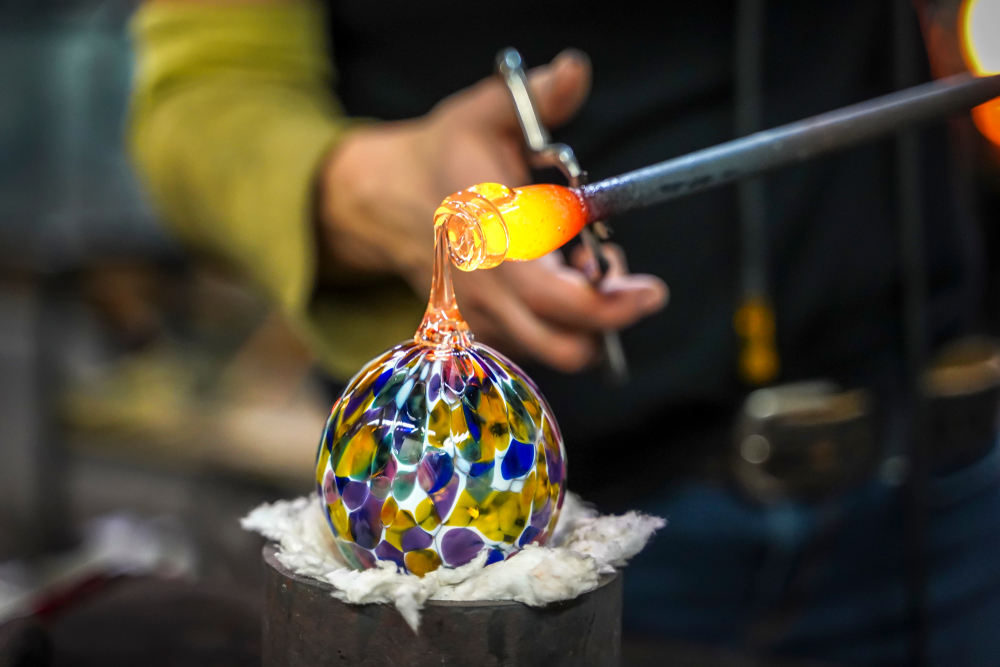 Glass blower working on  colorful orb of hot glass.