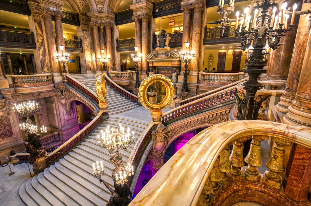 The Grand Staircase in the Palais Garnier with many ornate details and candelabras.