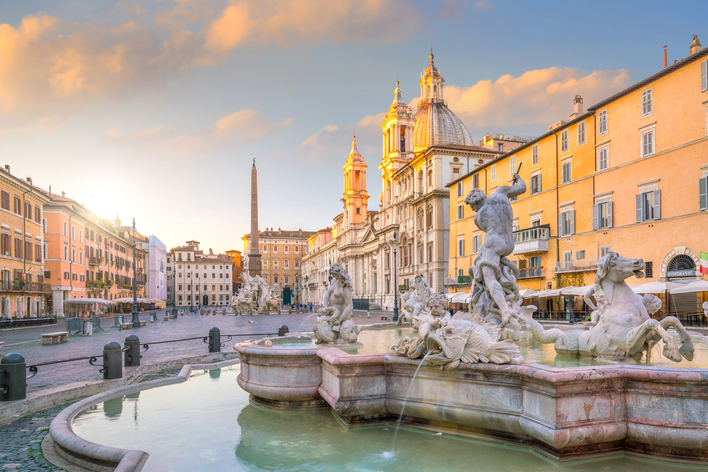 Piazza Navona at sunset with a fountain and yellow buildings.