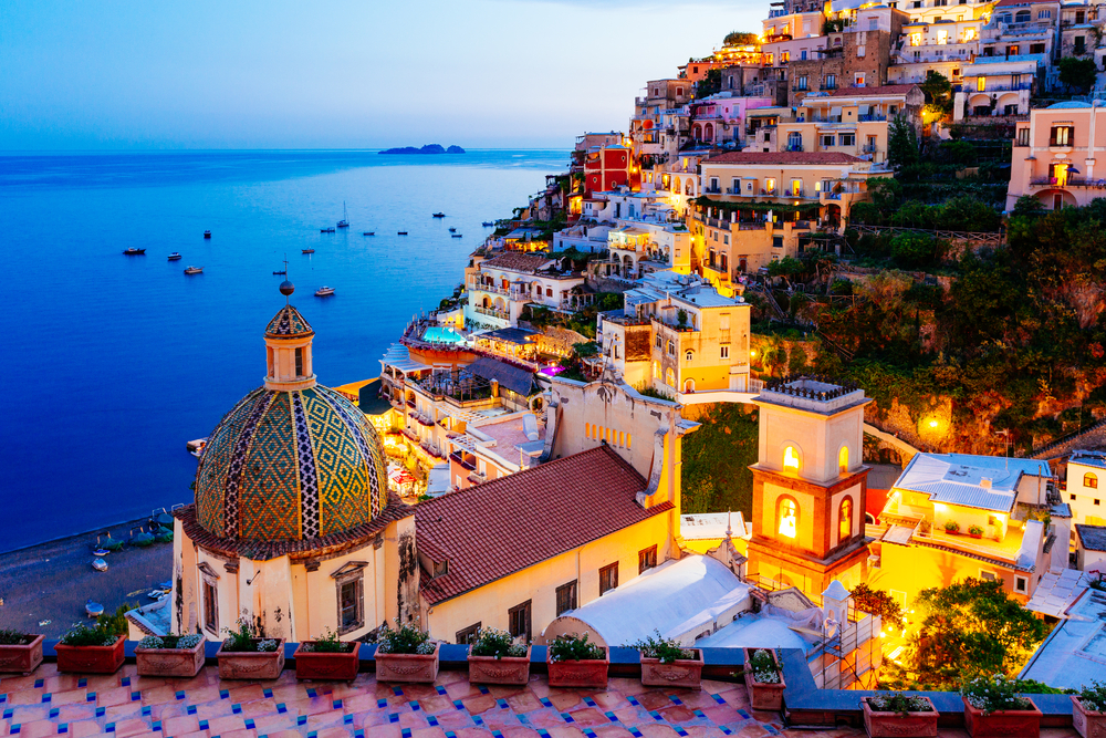 Twilight over the lit up buildings of Positano on a hill overlooking the ocean.