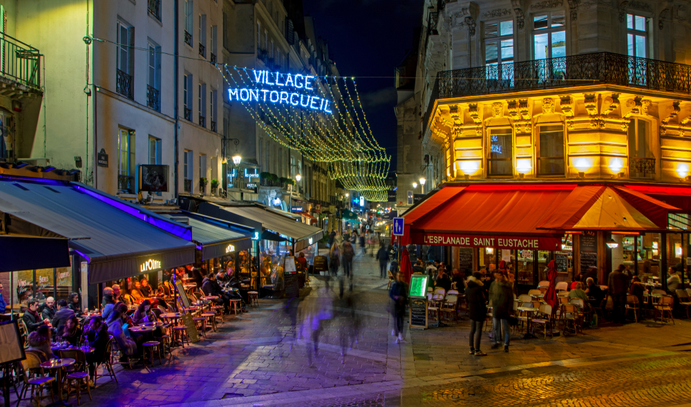 Nighttime at Rue Montorgueil with people walking or sitting at tables outside of restaurants.