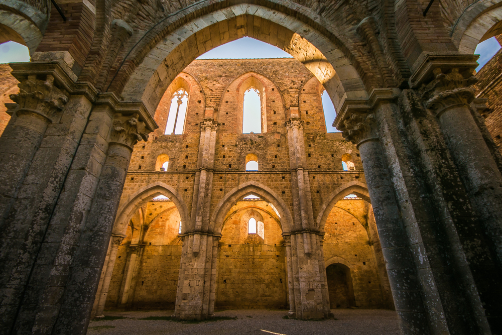View through an archway at golden light filling San Galgano Abbey in Italy.