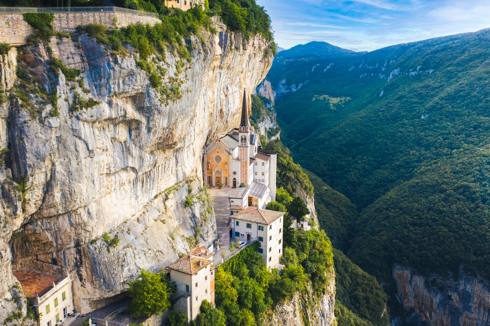 Aerial view of Santuario Madonna Della Corona hugging a sheer cliff overlooking the mountains.