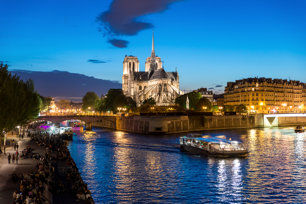 Boat gliding down the Seine River near Notre Dame at dusk.