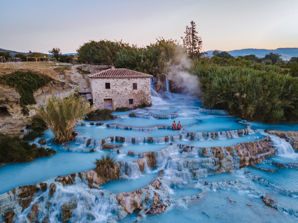 Aerial view of the tiered hot springs of Terme di Saturnia with blue water and waterfalls.
