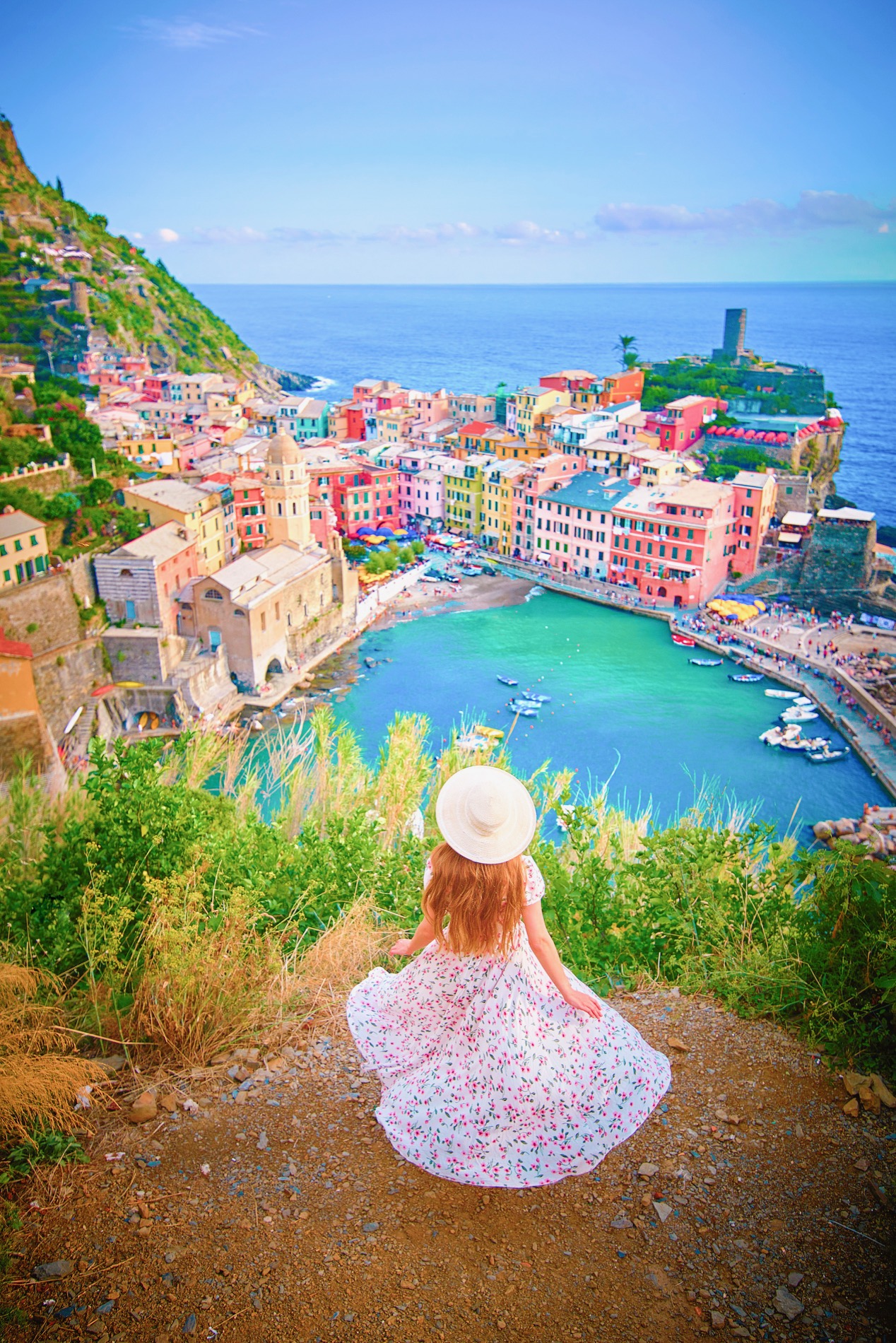 Woman in a floral dress looks out over the colorful town of Vernazza and its harbor.