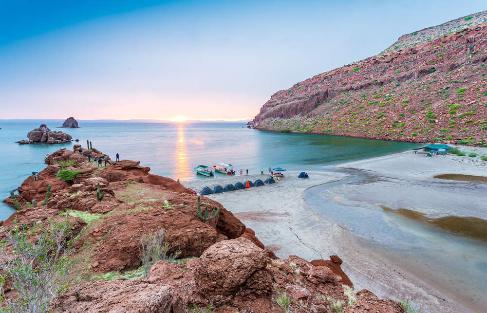 Champagne Beach, as shown as a cove in this photo with reddish rocks surrounding bubbly sand and blue waters during sunset, is one of the best beaches in the world! 