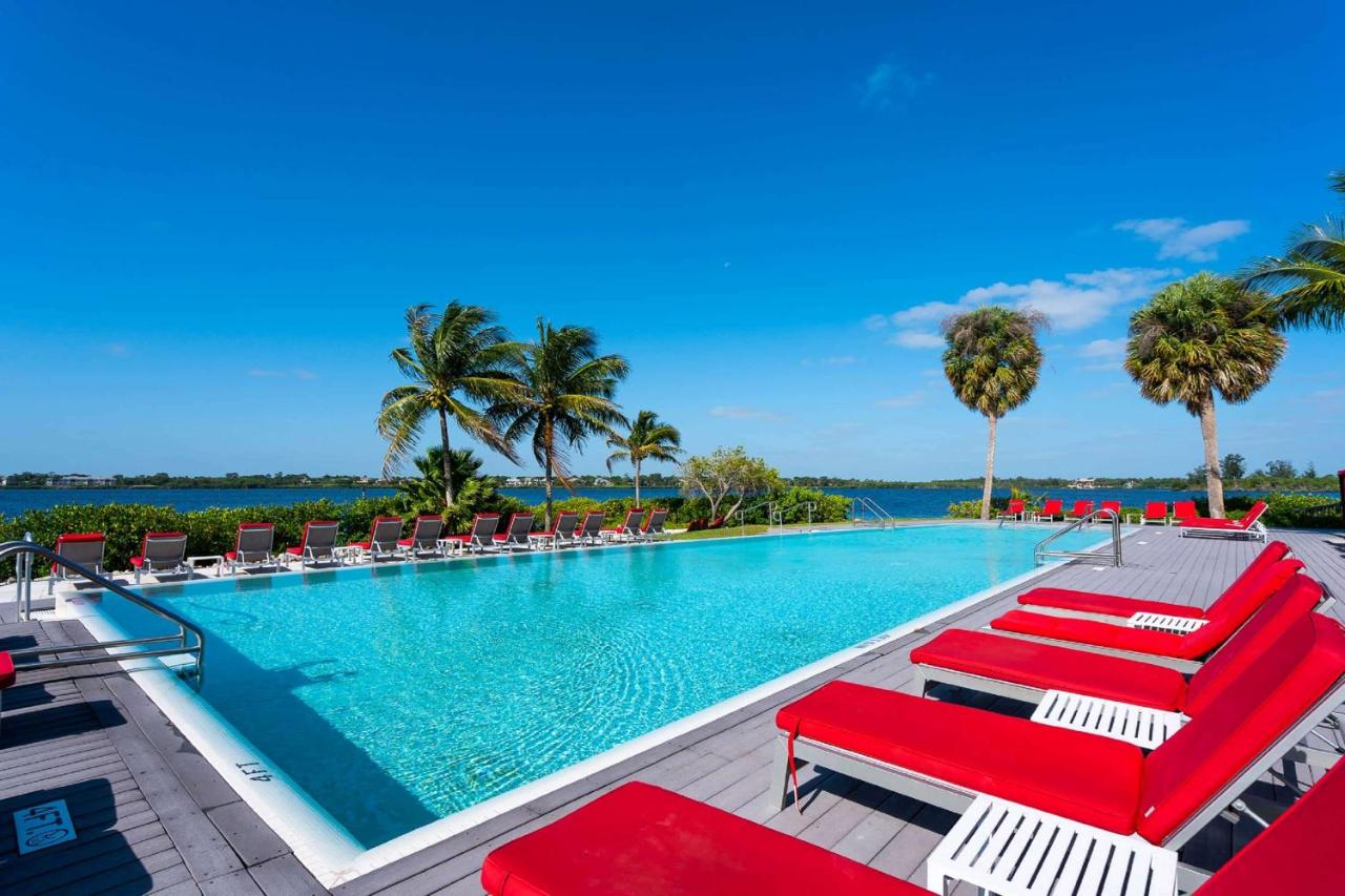 A bright blue pool surrounded by bright red lounge chairs and palm trees on a sunny day