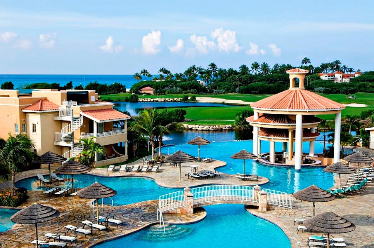 A series of pools and a lounge deck next to a golf course on the ocean at a Caribbean resort