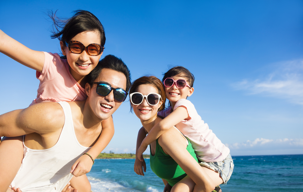A family of four on a beach wearing sunglasses. The kids are piggyback 