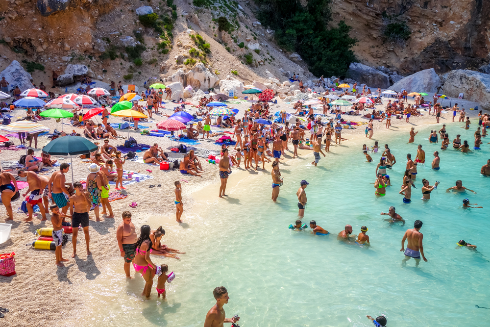 Tons of people crowd the white sand and blue water beaches on the coast of Italy in may.