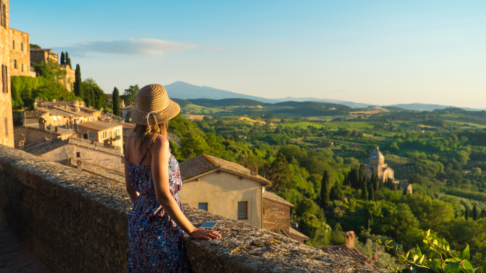 A woman looks over the rolling, green hills of Tuscany in Italy in May from the view point of a balcony.