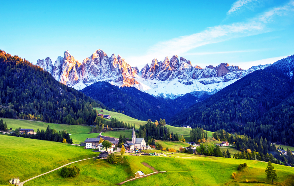 The Dolomites hover over green landscapes, but despite the rolling hills, the mountains are covered in snow already.
