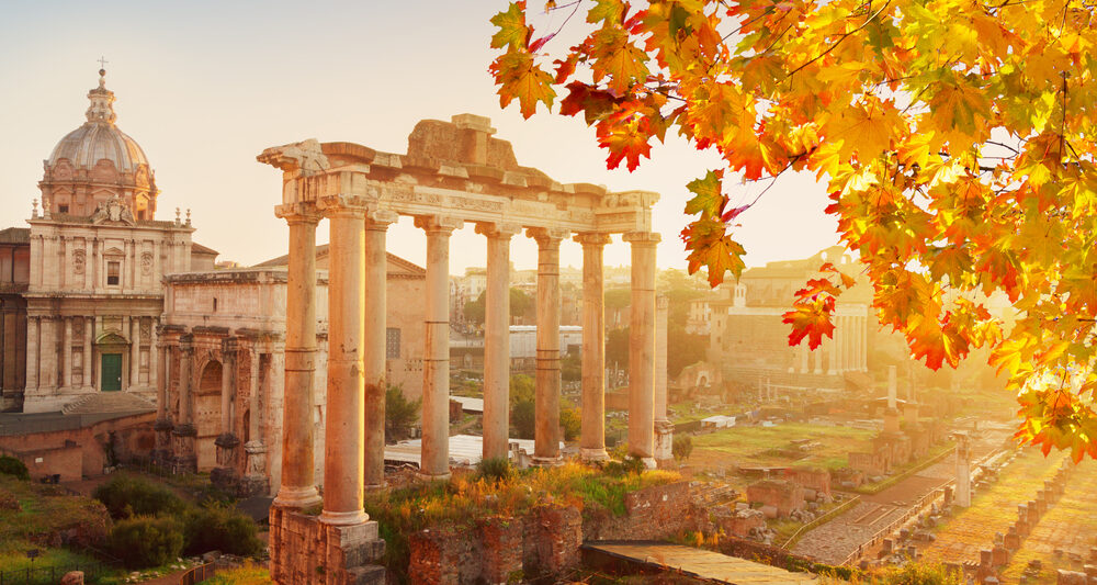 Ruins in Rome are a caught in the sunlight of this photo, with leaves of a nearby tree turning yellow with the upcoming autumn months.