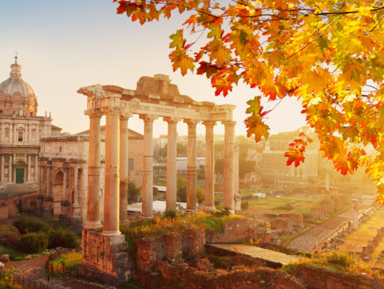 Ruins in Rome are a caught in the sunlight of this photo, with leaves of a nearby tree turning yellow with the upcoming autumn months.