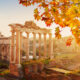 Ruins in Rome are a caught in the sunlight of this photo, with leaves of a nearby tree turning yellow with the upcoming autumn months.