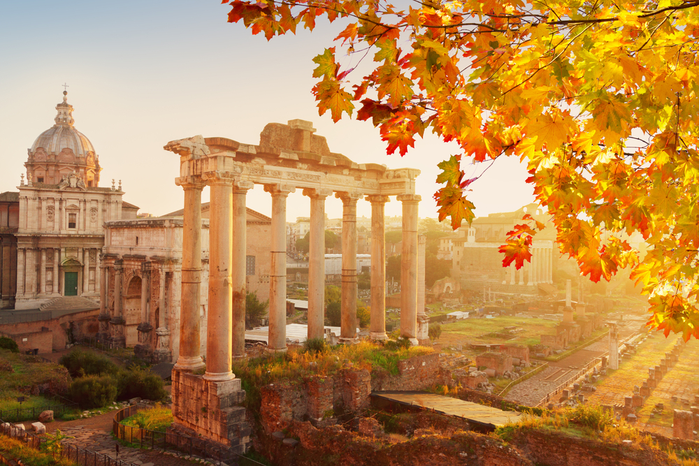 Fall comes in Italy in October with crisper leaves, brighter colors, and cooler weather, as seen in this photo of a monument in the sunset with fall leaves in the top right corner. 