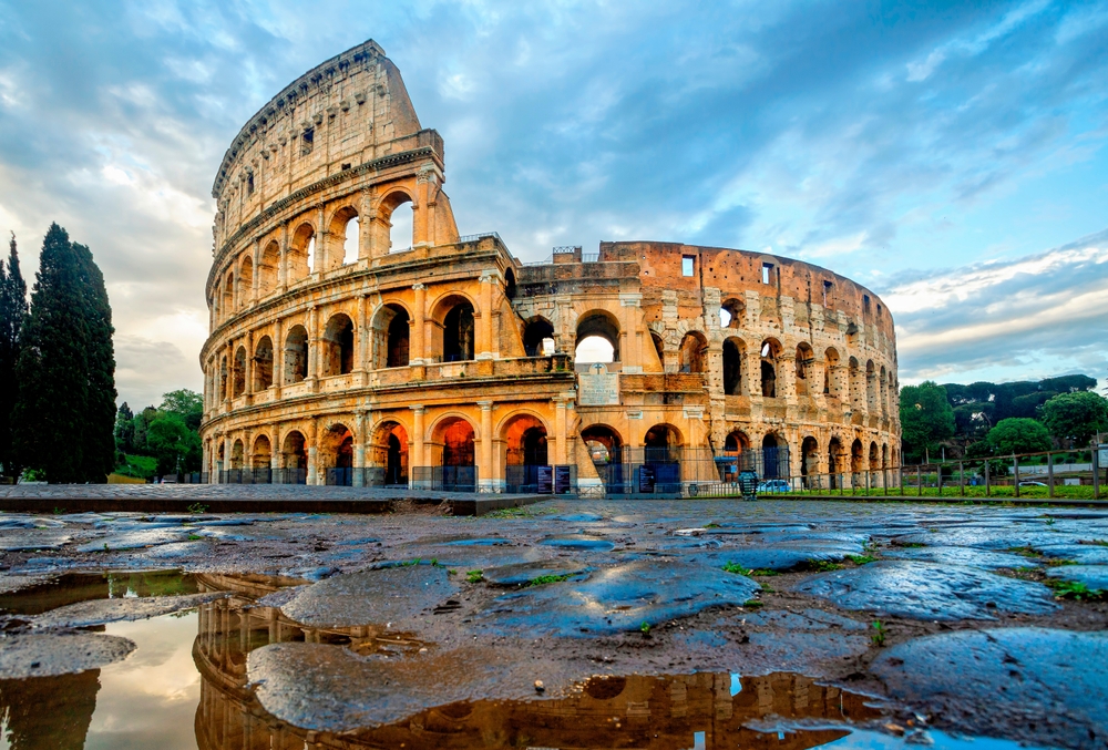 In Italy in October, the rain picks up, so areas see more participation, as shown in this photo. The Colosseum reflects in the puddles of water on the ground that surrounds it.