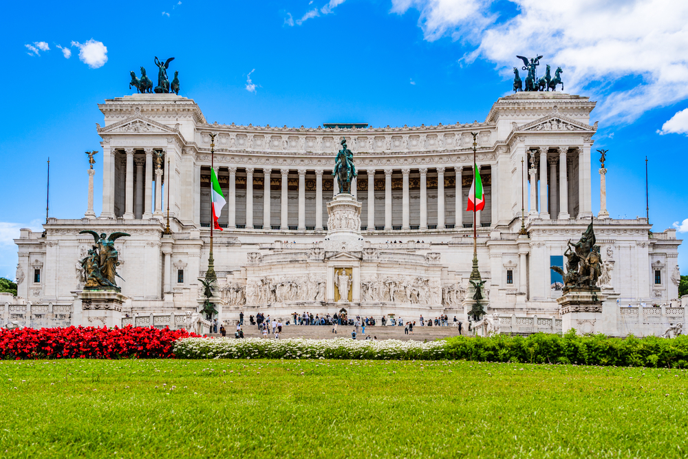 View across grass to the Altar of the Fatherland with Italian flags flying.