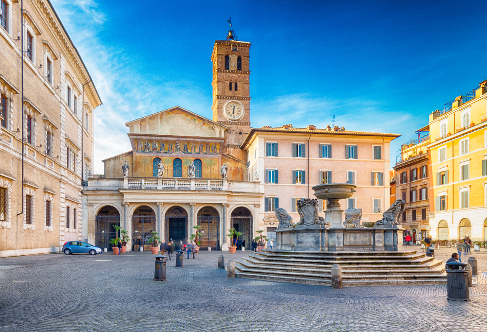 Exterior of the Basilica of Santa Maria in Trastevere with a square and fountain in front.