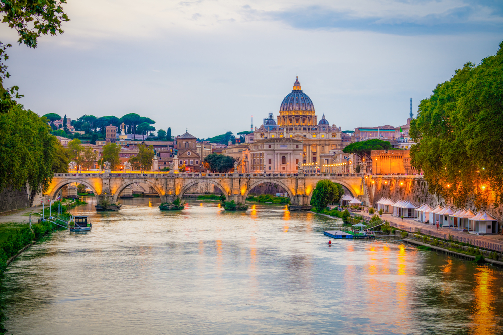 Sunset over the Tiber River and a bridge with the Vatican in the distance.