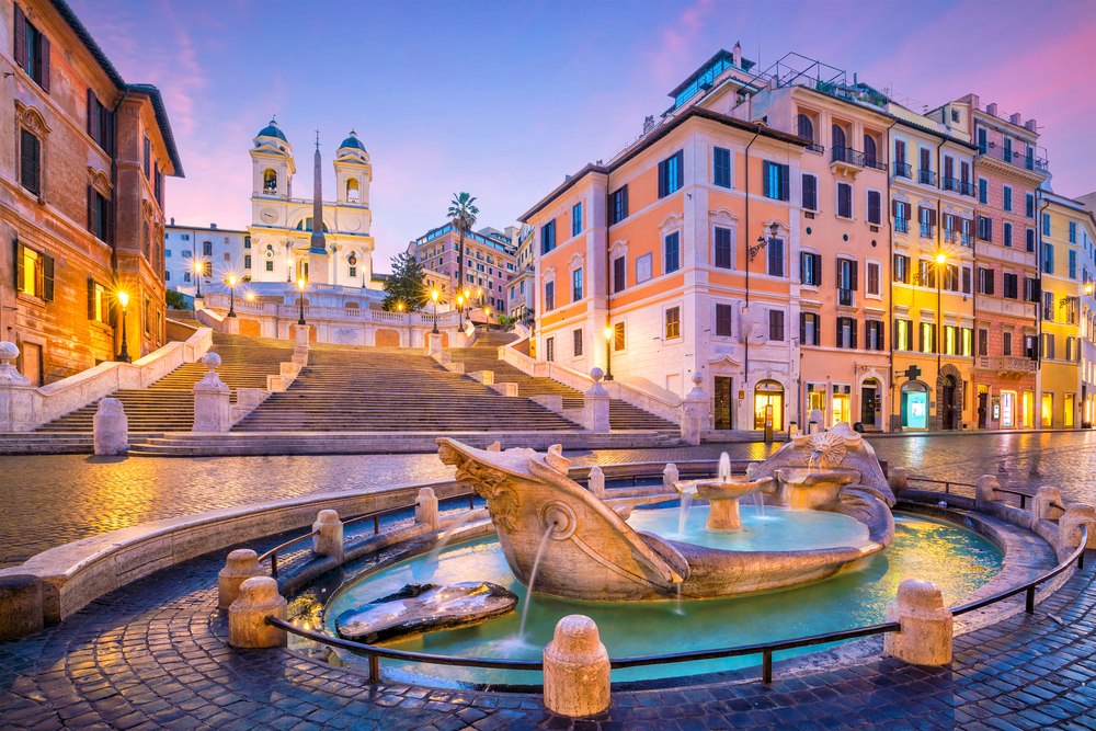 Purple and pink sunrise over the Spanish Steps with a fountain in the square in front.