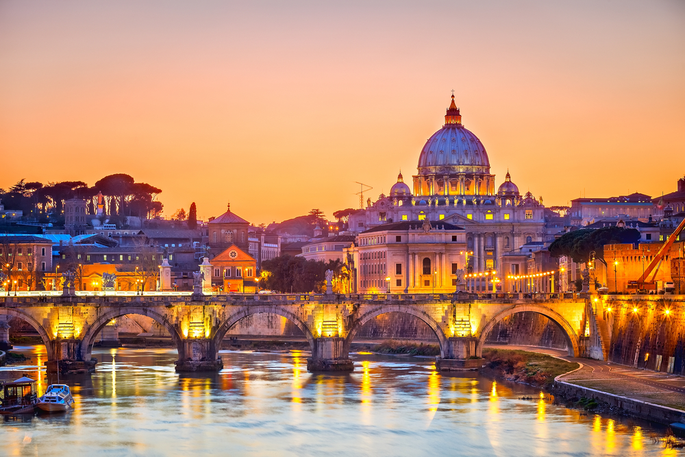 Orange dusk over the river with a bridge and St. Peter's Basilica lit up during 4 days in Rome.