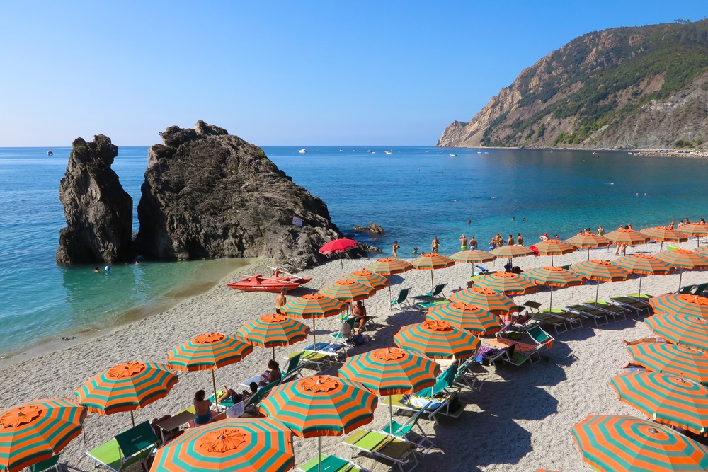 Colorful beach umbrellas snake across the beach at Monterosso al Mare on Italy’s Cinque Terre coast. The article is aboutthe best time to visit Italy.