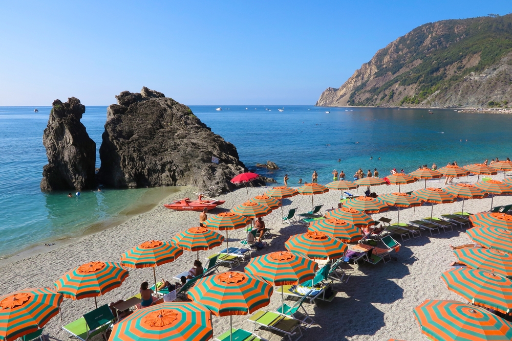 Colorful beach umbrellas snake across the beach at Monterosso al Mare on Italy’s Cinque Terre coast. The article is aboutthe best time to visit Italy. 