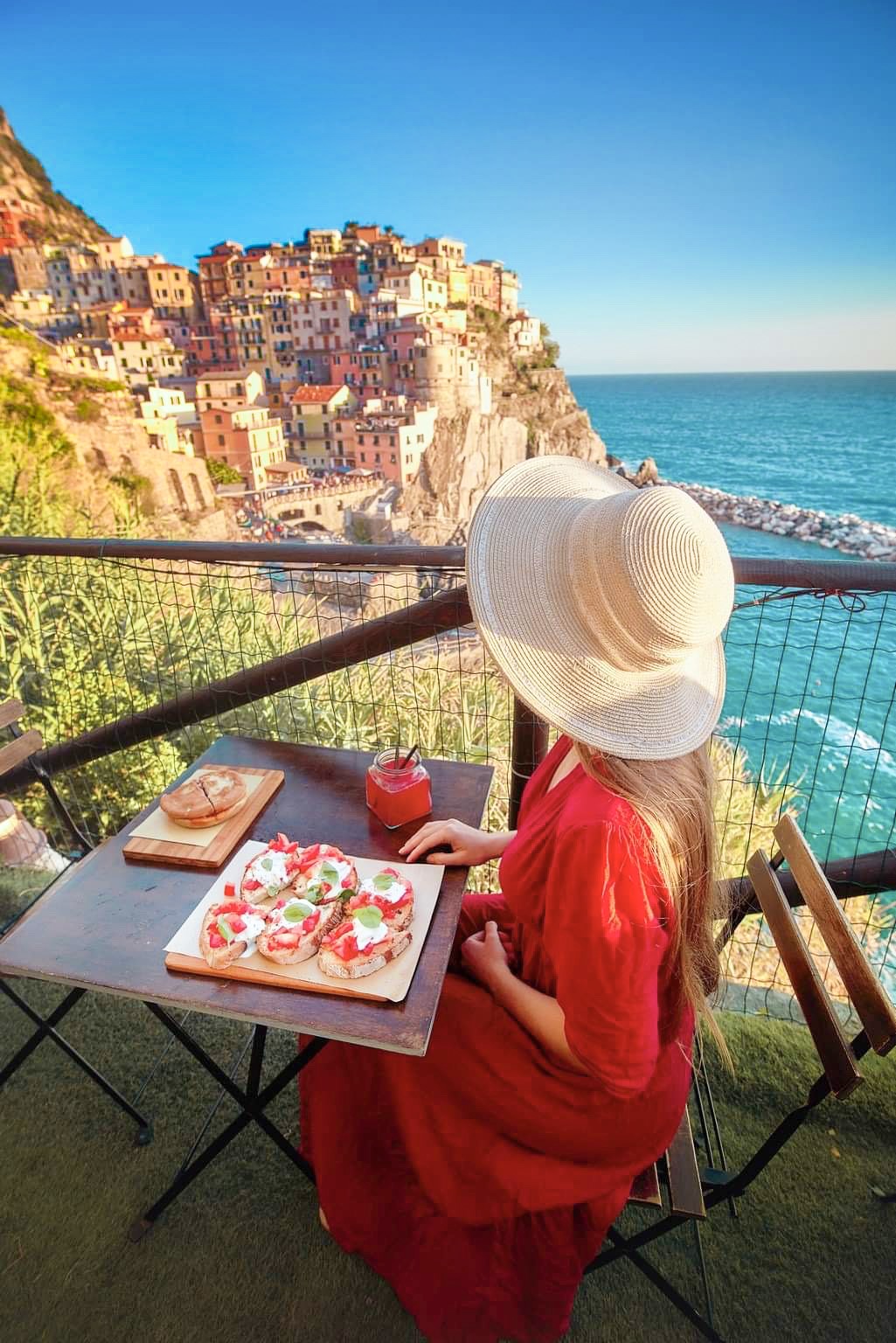 Girl sat in a cafe looking out over an Italian coastal town. She is wearing a red dress.