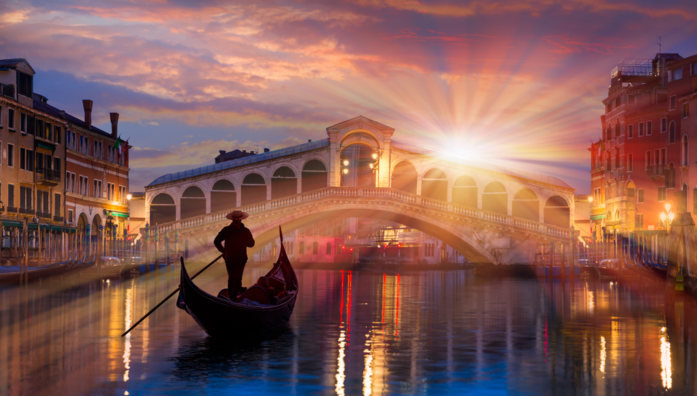 Gondola near Rialto Bridge in Venice, Italy at sunset with sun setting. The article is about the best time to visit Italy.  